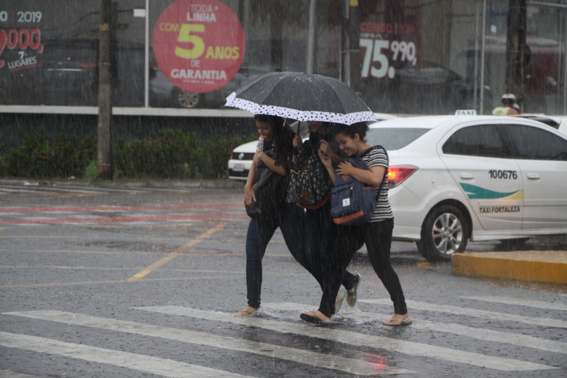 Trio divide solidariamente guarda-chuva na tentativa de se molhar o mínimo possível