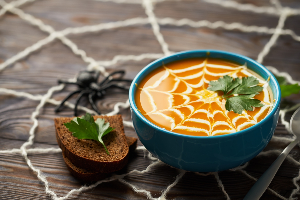 A healthy pumpkin puree garnished with cream and parsley leaves. Composition autumn cream soup with toys for the holiday Halloween on a dark wooden background (Foto: Getty Images/iStockphoto)
