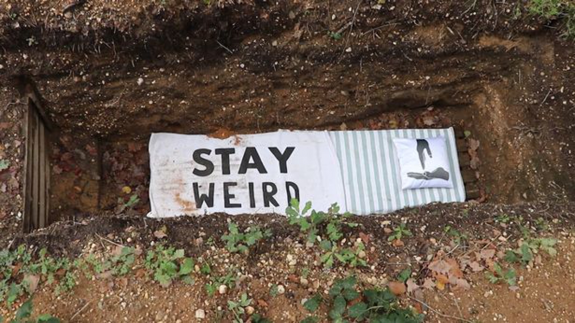 No fundo do túmulo, apenas uma toalha com os dizeres "Stay Weird" (Fique estranho, em tradução literal) forra o buraco