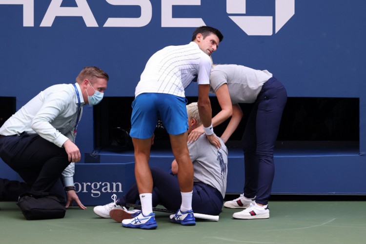 Novak Djokovic ajuda no socorro à juíza de linha que ele atingiu com uma bolada no pescoço. O sérvio foi eliminado do US Open pelo episódio