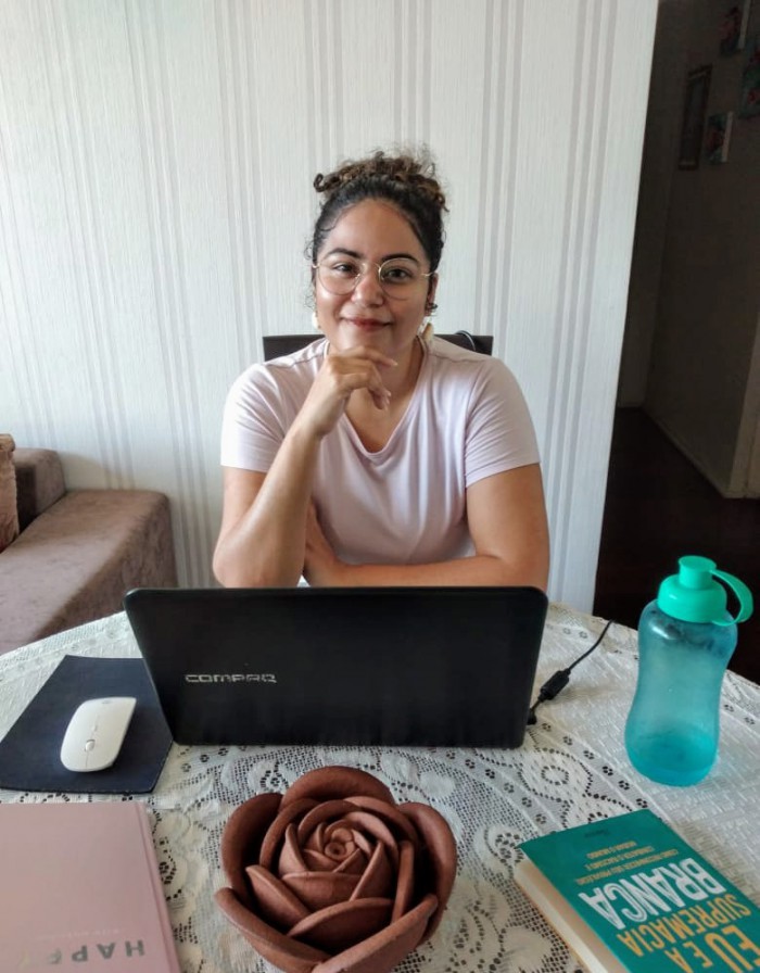 Izabel sentada à mesa com seus companheiros de trabalho: notebook, mouse e garrafa d’água