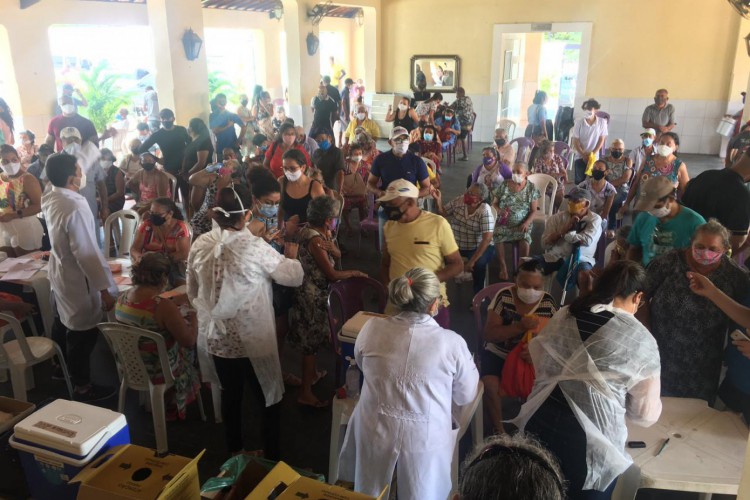Vacinação para idosos a partir de 72 anos neste sábado, em Caucaia. Abatida, dona Tecla não quis uma foto só dela. Na imagem ela aparece bem ao fundo, do lado esquerdo, com roupa e máscara azuis e detalhes em vermelho