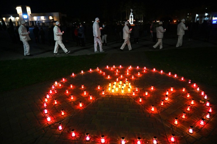 Funcionários da usina de Chernobyl carregam velas perto da placa de radioatividade no monumento às vítimas de Chernobyl em Slavutych, a cidade onde o pessoal da usina morava, a cerca de 50 quilômetros (30 milhas) do local do acidente