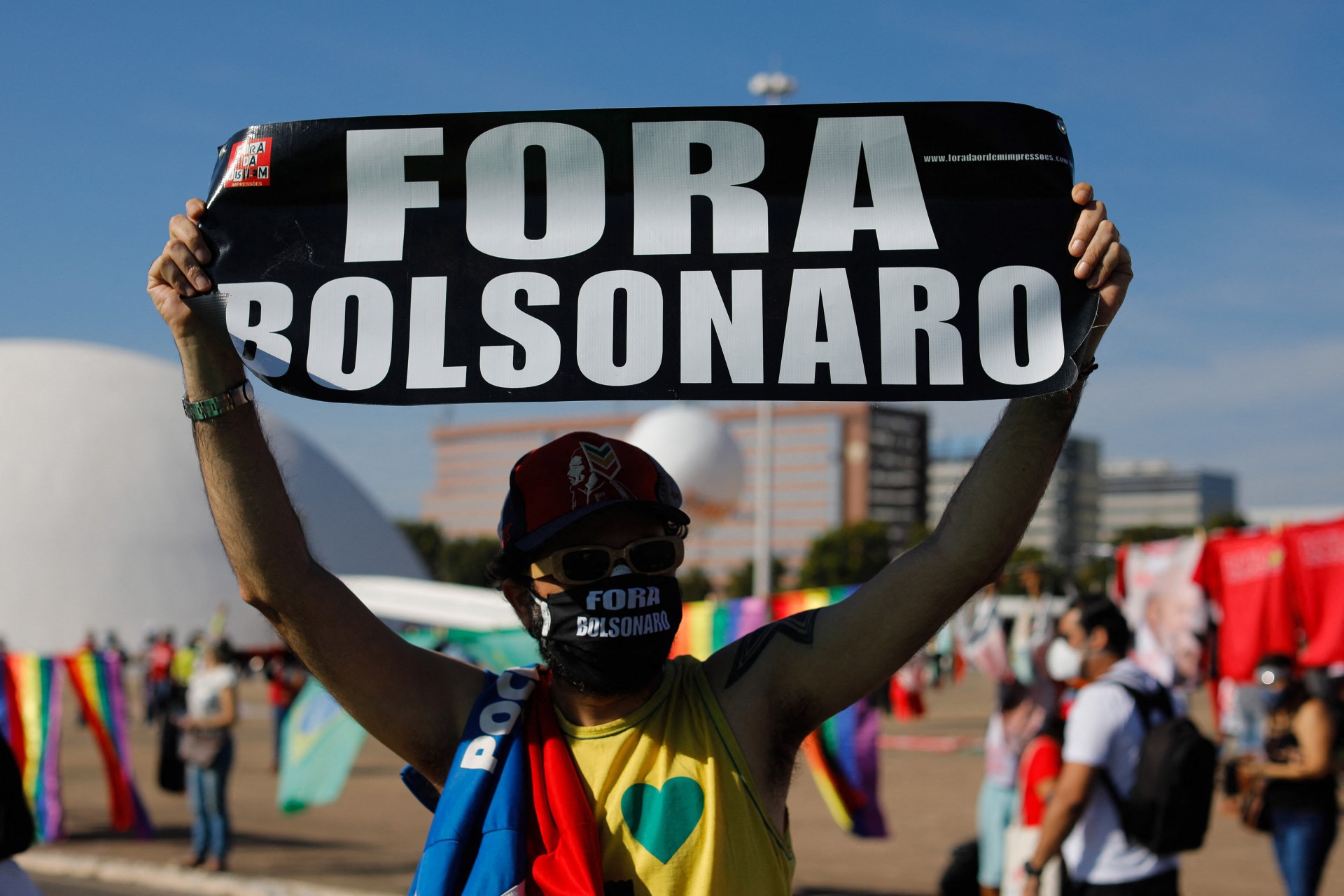 An activist holds a sign during a protest by opposition parties and social movements against Brazilian President Jair Bolsonaro's handling of the COVID-19 pandemic in Brasilia, on June 19, 2021. - Far-right President Jair Bolsonaro has been facing criticism for his management of the pandemic, including initially refusing offers of vaccines, as epidemiologists warn Brazil may now be on the brink of a third wave of Covid-19. (Photo by Sergio Lima / AFP)       Caption