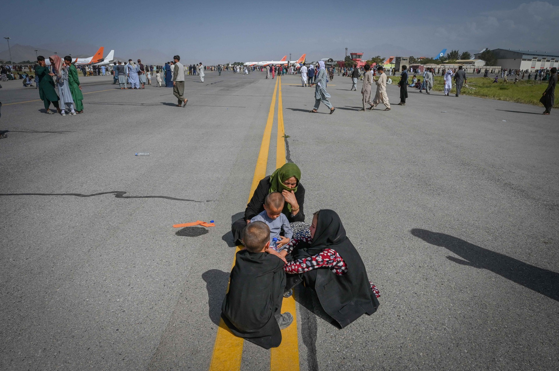 Povo afegão senta-se na pista enquanto espera para deixar o aeroporto de Cabul, após um fim incrivelmente rápido para a guerra de 20 anos do Afeganistão, enquanto milhares de pessoas tentavam fugir da temida marca linha-dura do Talibã (Foto: WAKIL KOHSAR / AFP)