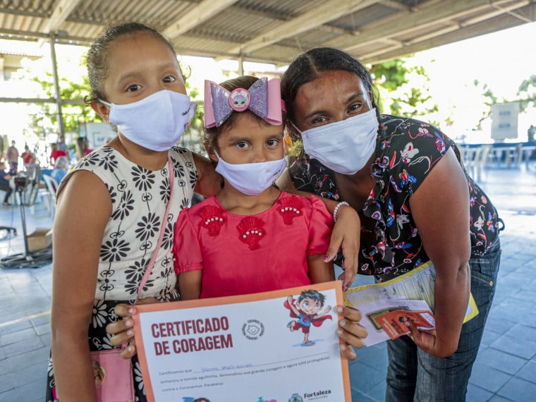 Irene, de 7 anos, mostra o "certificado de coragem" que recebeu após tomar primeira dose da vacina contra a Covid-19. Ela estava acompanhada da mãe, Gisele Gomes da Silva, 29, e da irmã mais velha, Vitória, 9