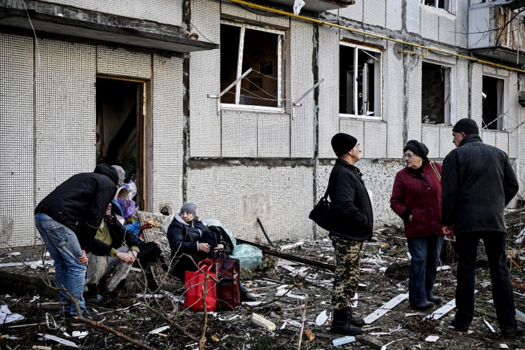 Pessoas ficam do lado de fora de um prédio destruído após bombardeios na cidade de Chuguiv, no leste da Ucrânia, em 24 de fevereiro de 2022, enquanto as forças armadas russas tentam invadir a Ucrânia de várias direções. 