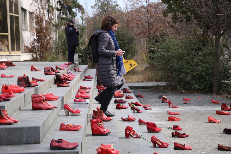 Uma mulher passa por uma instalação de sapatos femininos vermelhos exibidos em uma escada, como símbolo de denúncia da violência contra as mulheres, na praça principal de Tirana, no Dia Internacional da Mulher, em 8 de março de 2022. 