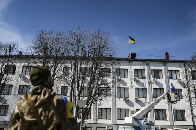 Um militar olha para a bandeira ucraniana hasteada por um funcionário na prefeitura de Bucha, oeste de Kiev, em 7 de abril de 2022