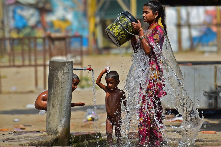 Mulher junto com uma criança toma banho em uma torneira de beira de estrada em um dia quente de verão em Allahabad em 28 de abril de 2022.