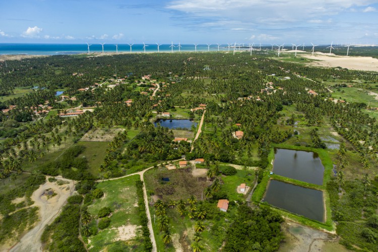 Vista aérea do assentamento Barra de Moitas, em Amontada, que fica próximo ao encontro do rio Aracatiaçu com o mar. Ao fundo, os parques eólicos instalados na região(Foto: FCO FONTENELE/O POVO)