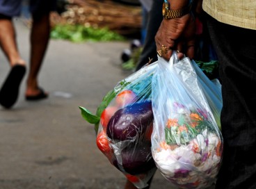 Um homem carrega flores e legumes em sacos plásticos descartáveis ​​em um mercado local em Calcutá em 1º de julho de 2022 
