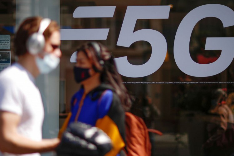 People, wearing protective face masks, walk past a 5G data network sign at a mobile phone store in Paris, France, April 22, 2021. REUTERS/Gonzalo Fuentes