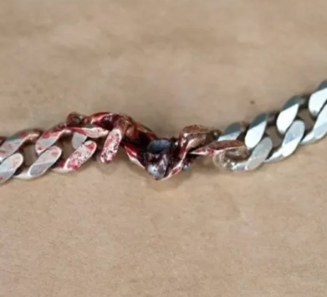 Segundo a polícia, a corrente de 10 mm de espessura não era de prata pura, pois a maciez fez com que absorvente a bala. Imagem mostra o projétil de calibre 22 alojado na corrente, manchada de sangue da vítima.