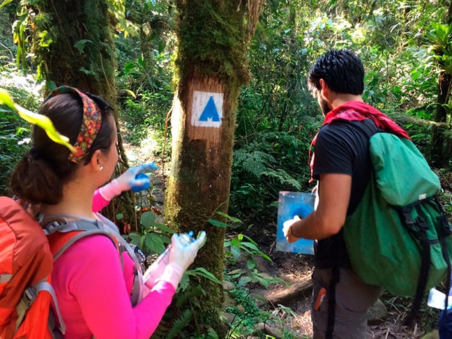 Eles usam estêncil para aplicar uma pintura rústica. E fica mais fácil carregar o material para a sinalização sem prejudicar a natureza. 