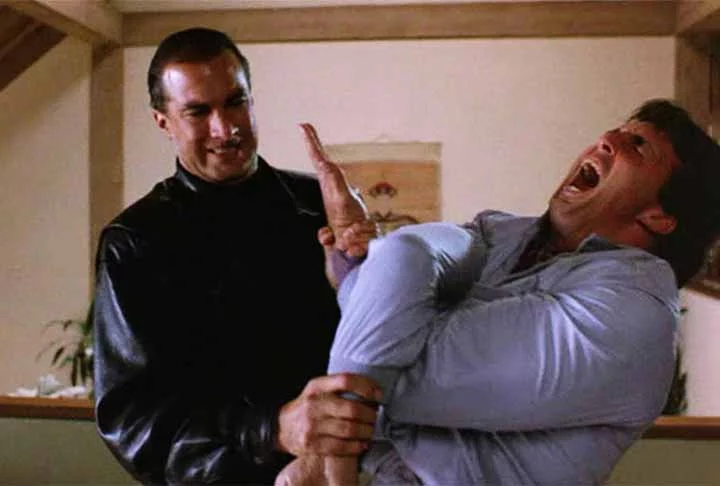 Steven Seagal, conhecido por sua abordagem polêmica e controversa, ganhou fama no final dos anos 80 com Nico: Acima da Lei, tornando-se uma estrela da Era-Kickboxing. Embora seu estilo de artes marciais, o Aikido, fosse mais sutil comparado aos socos e chutes exagerados da época, Seagal se destacou em filmes de ação e conquistou o apelido de “invencível” devido à sua representação de personagens que nunca se feriam.