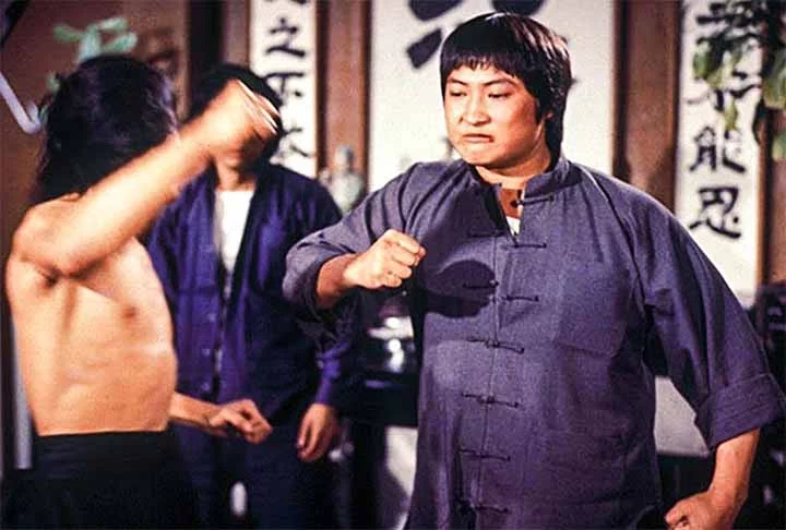 O mais velho dos Três Irmãos, Sammo Hung, é uma lenda das artes marciais. Com um Kung Fu excepcional, ele provou que peso não define a habilidade em combate. Sua combinação de humor e técnica nas lutas cativou audiências globalmente, destacando seu profundo conhecimento em artes marciais. Hung dirigiu muitos dos filmes de Jackie Chan nos anos 80, trazendo uma famosa mistura de ação e comédia. Como coreógrafo e diretor, ele inovou no uso de dublês, introduzindo novos truques que elevaram o níve