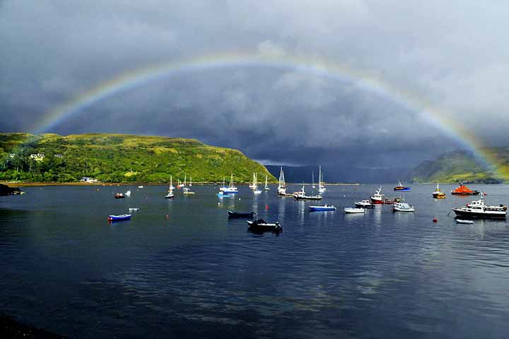 Ilha de Skye - Cidade: Escócia-  O clima frequentemente chuvoso e a luz solar intermitente criam condições ideais para a formação de arco-íris sobre as paisagens montanhosas e dramáticas da Ilha de Skye, tornando-a famosa pelos arcos vibrantes que contrastam com o céu nublado.
