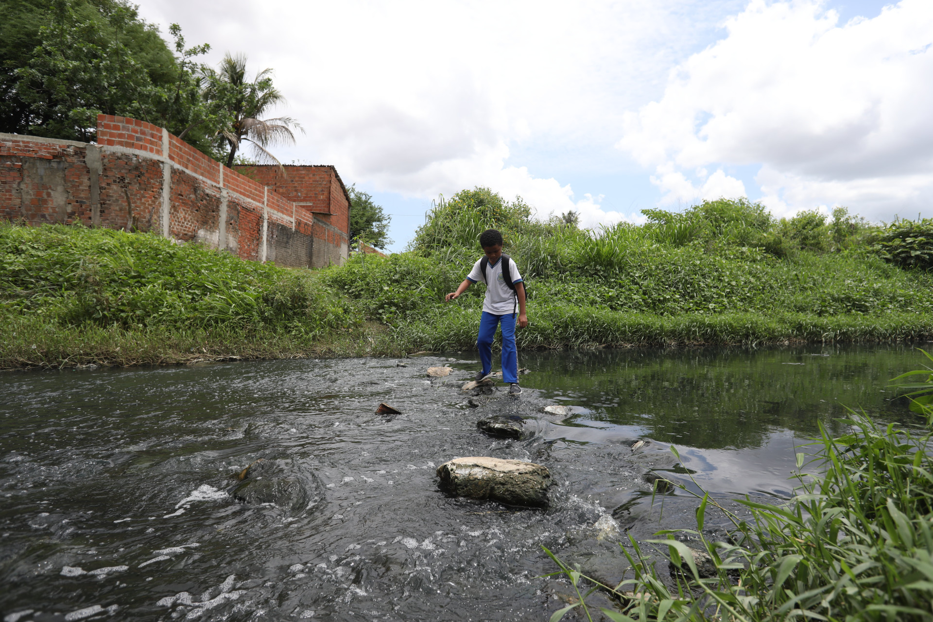 Estudantes e moradores atravessam c&oacute;rrego, por falta de ponte sobre o rio Maranguapinho 