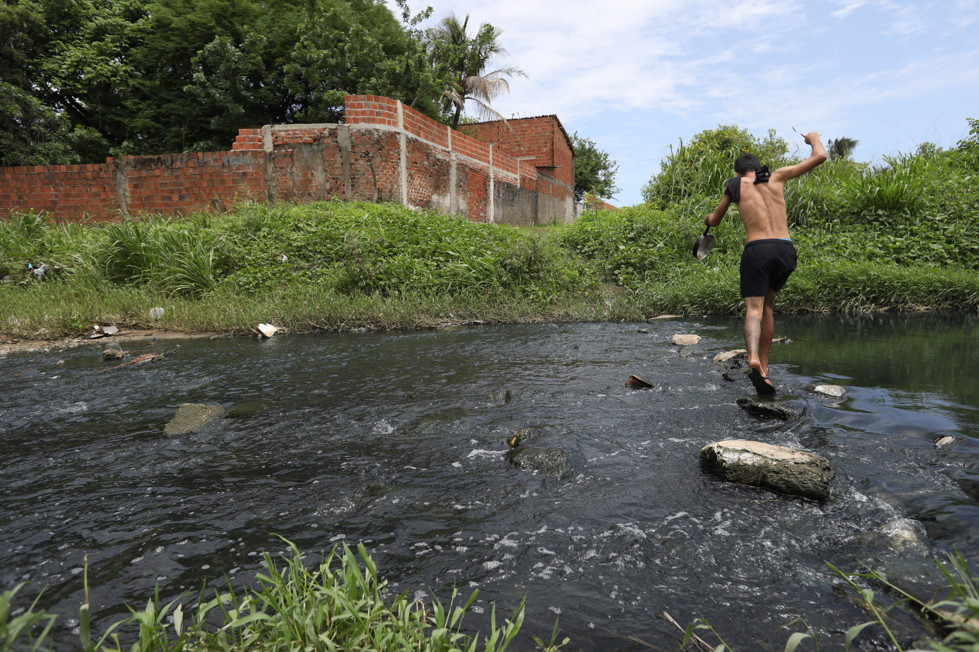 Estudantes e moradores atravessam c&oacute;rrego, por falta de ponte sobre o rio Maranguapinho 