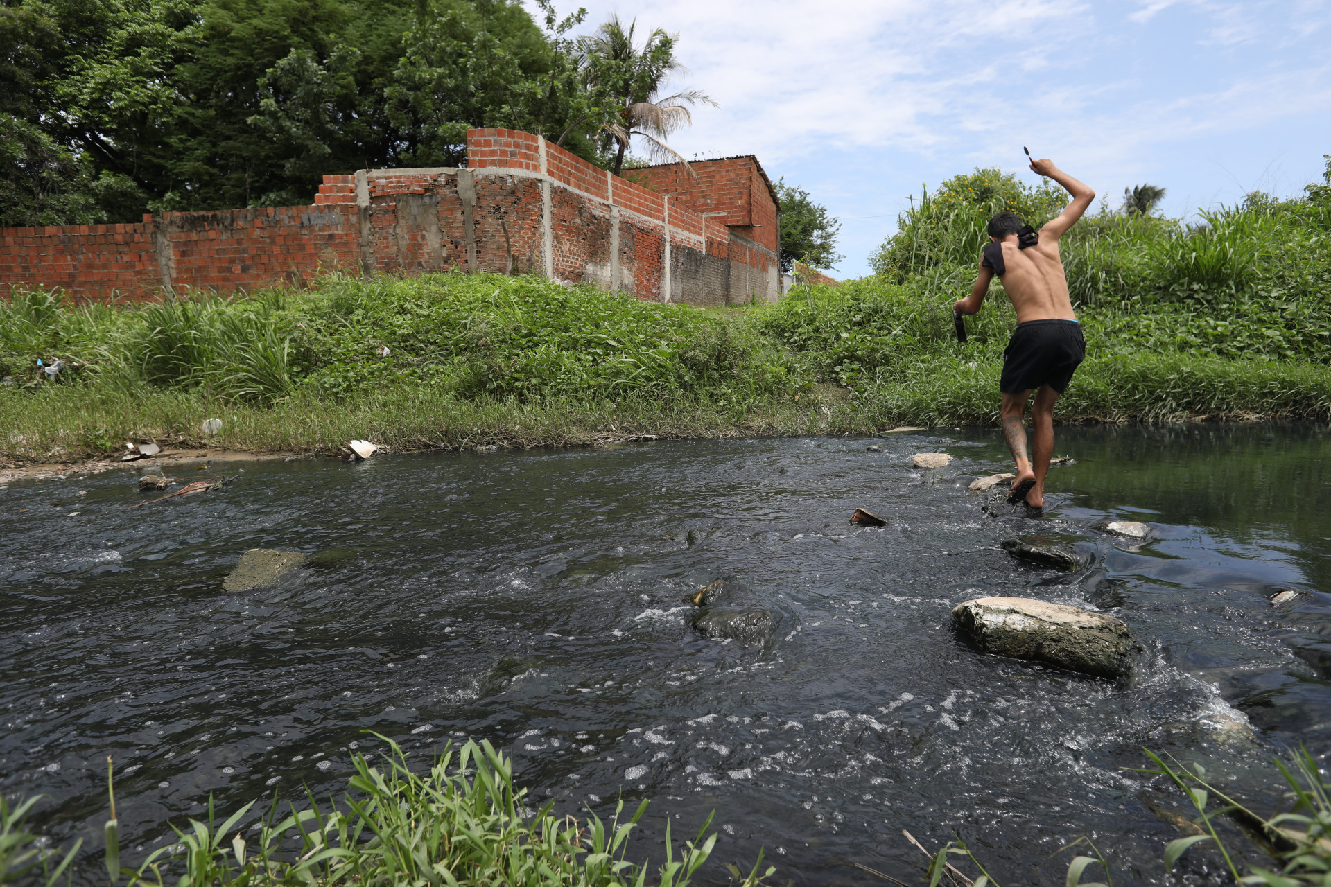 Estudantes e moradores atravessam c&oacute;rrego, por falta de ponte sobre o rio Maranguapinho 