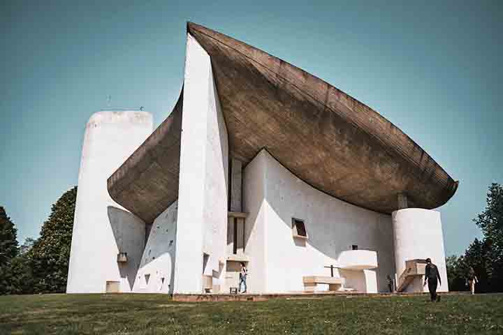 Capela de Ronchamp (França) – 1954 - Projetada por Le Corbusier, tem formas curvas e assimétricas inovadoras. Pequenas aberturas na parede criam um jogo único de luz. Apesar da simplicidade, transmite paz e introspecção.
