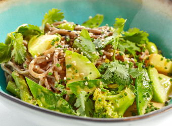 Healthy pasta soba with green vegetables. Vegetarian dish - soba with zucchini, broccoli and green pea on ceramic bowl. Veggie food handmade bowl isolated on white background. Plant based bowl dining