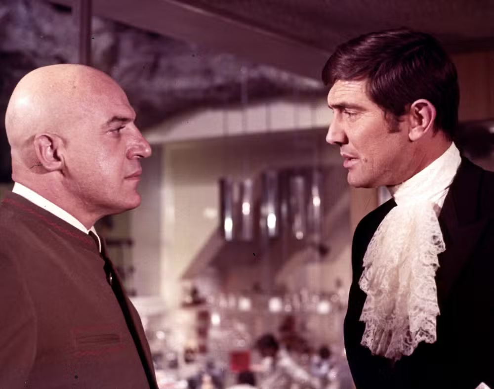 Lazenby ganhou fama ao interpretar o agente secreto James Bond em 007 A Serviço Secreto de Sua Majestade, em 1969. É o único ator que viveu o personagem apenas uma vez. Mas o papel alçou sua carreira na época. Na foto, ele (direita) em cena com Telly Savallas. 