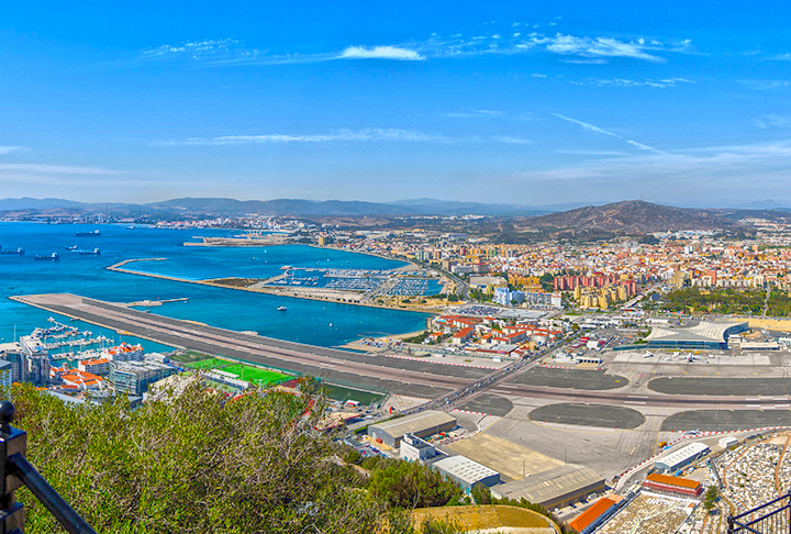 A pista do aeroporto corta uma das principais estradas de uma área urbana densamente povoada. Carros e pedestres precisam esperar enquanto os aviões decolam ou aterrissam. 