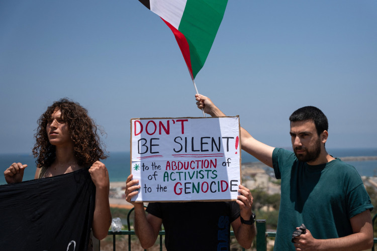 Manifestantes seguram cartazes e a bandeira palestina durante um encontro perto do porto israelense de Ashdod, em 9 de junho de 2025, ap&oacute;s for&ccedil;as israelenses interceptarem um barco de ajuda humanit&aacute;ria com destino a Gaza