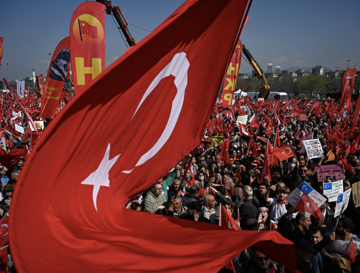 Esta fotografia mostra uma enorme bandeira nacional turca tremulando sobre manifestantes durante uma manifestação convocada pelo Partido Republicano do Povo (CHP) em apoio à prisão do prefeito de Istambul, Ekrem Imanoglu, em Maltepe, nos arredores de Istambul, em 29 de março de 2025.