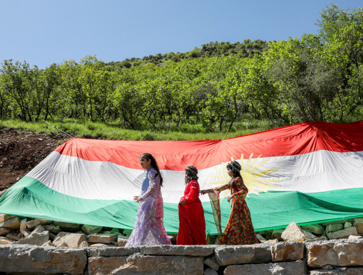 Crianças passam por uma bandeira curda gigante durante uma celebração da minoria religiosa Kakai, do Curdistão iraquiano, do 