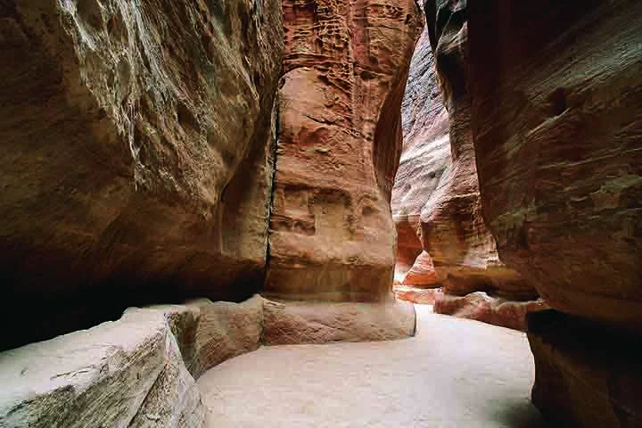 O acesso a Petra já é, por si só, uma experiência memorável. Para chegar ao coração da cidade, os visitantes percorrem o Siq, um estreito desfiladeiro de aproximadamente 1,2 km de extensão, ladeado por altas paredes de rocha que podem atingir até 80 metros de altura.