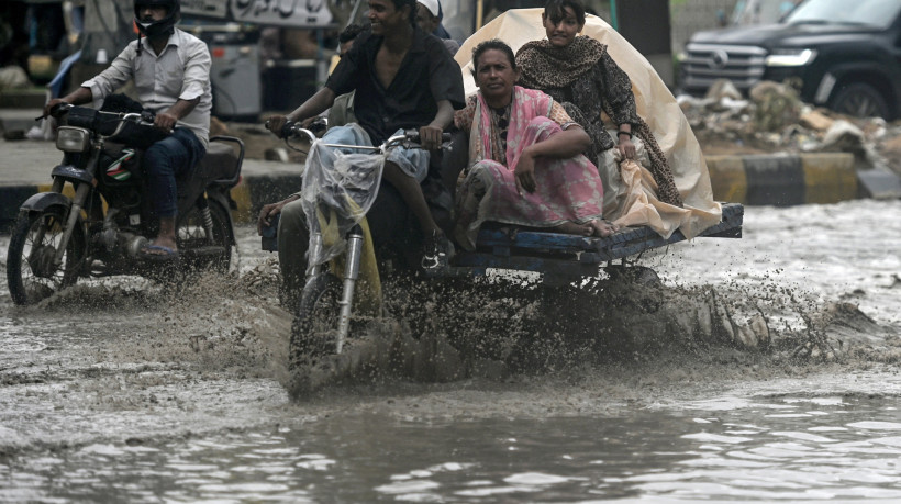 Passageiros atravessam uma rua inundada ap&oacute;s fortes chuvas em Karachi, em 28 de junho de 2025