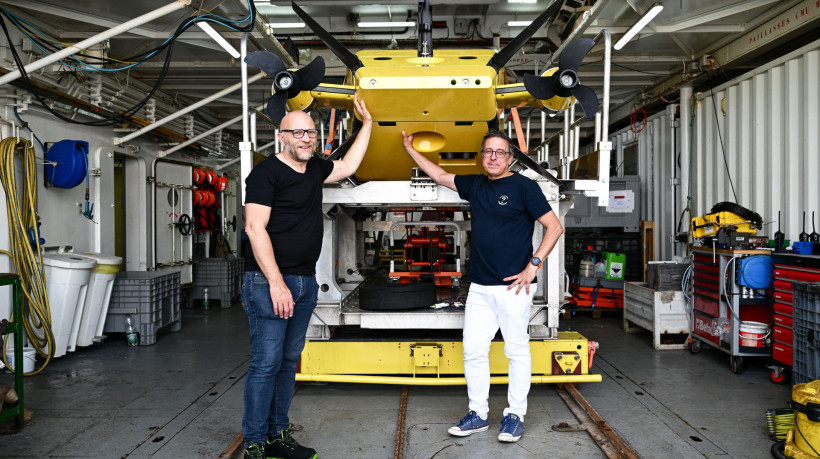Pesquisadores do CNRS e idealizadores do projeto Nodssum, Patrick Chardon (esquerda) e Javier Escartin (direita), posam ao lado do robô subaquático Ulyx a bordo do navio científico L'Atalante, atracado no porto de Brest antes da partida, em 15 de junho de 2025. Entre 1950 e 1990, mais de 200 mil barris cheios de rejeitos radioativos foram lançados no abismo do Oceano Atlântico Nordeste. A primeira missão da campanha Nodssum visa mapear a principal área de imersão dos barris e estudar as interações com a biodiversidade marinha