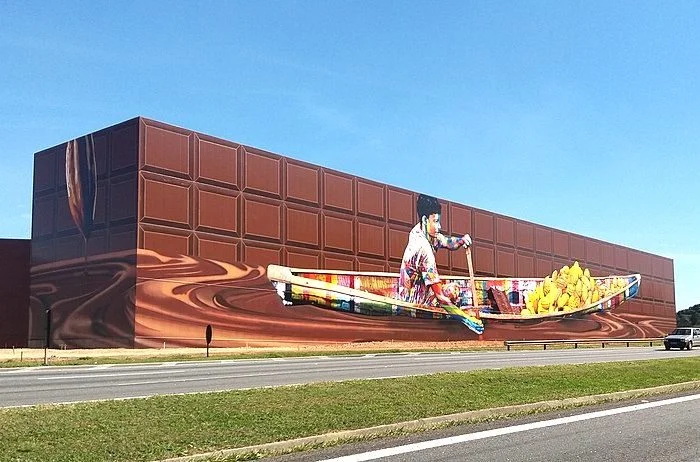 Quem passa pela rodovia Castelo Branco consegue ver a obra que estampa o prédio de uma fábrica de chocolate.  O mural de 5.742 metros quadrados retrata um coletor de cacau e, com tamanho gigantismo, garantiu o recorde mundial.