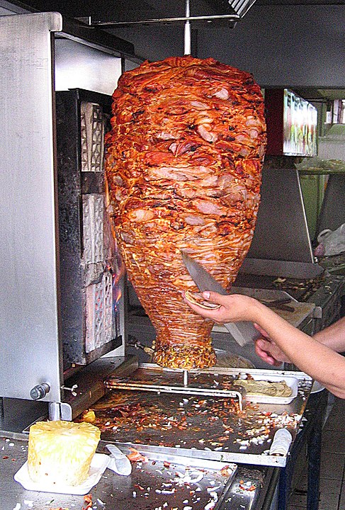 México - Tacos al Pastor: Carne marinada em uma mistura de pimentas, como guajillo e ancho, servida em tortilhas com abacaxi, cebola e coentro.

