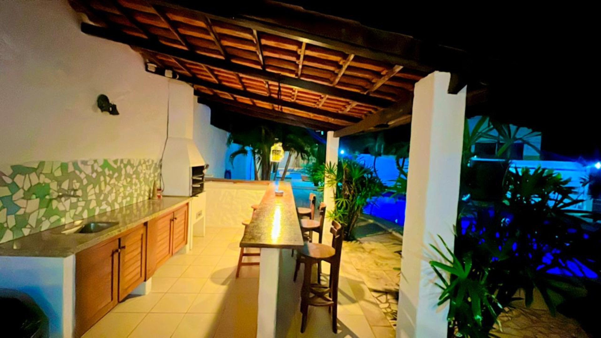 A estrutura inclui piscina, área de lazer com churrasqueira e bar, suítes equipadas com ar-condicionado, chuveiro aquecido por energia solar, escrivaninha, TV Smart, frigobar, e camas confortáveis