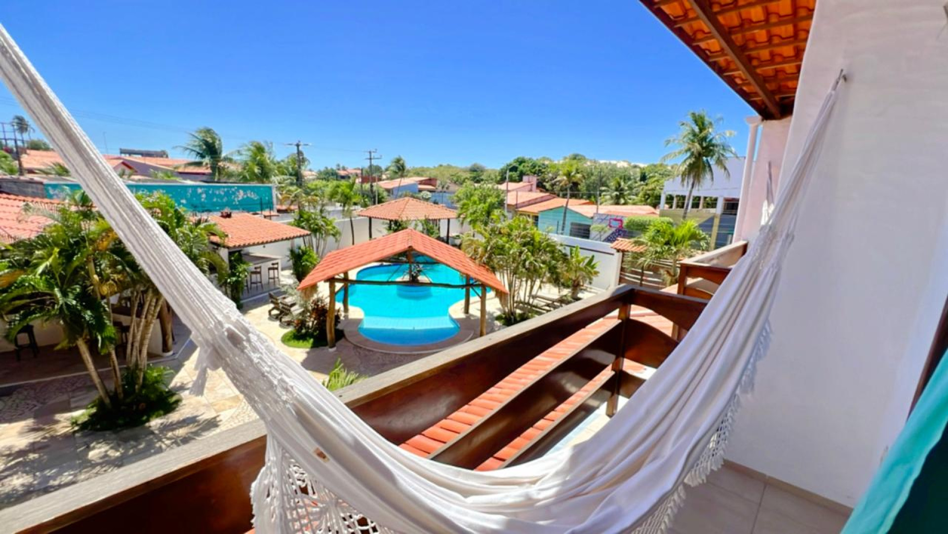 A estrutura inclui piscina, área de lazer com churrasqueira e bar, suítes equipadas com ar-condicionado, chuveiro aquecido por energia solar, escrivaninha, TV Smart, frigobar, e camas confortáveis