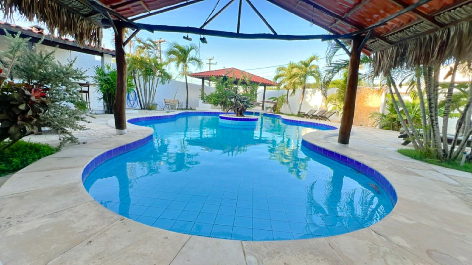 A estrutura inclui piscina, área de lazer com churrasqueira e bar, suítes equipadas com ar-condicionado, chuveiro aquecido por energia solar, escrivaninha, TV Smart, frigobar, e camas confortáveis