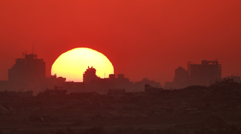 Foto tirada de um local na fronteira de Israel com a Faixa de Gaza, em 23 de julho de 2025, mostra o pôr do sol atrás de prédios destruídos dentro do território palestino sitiado