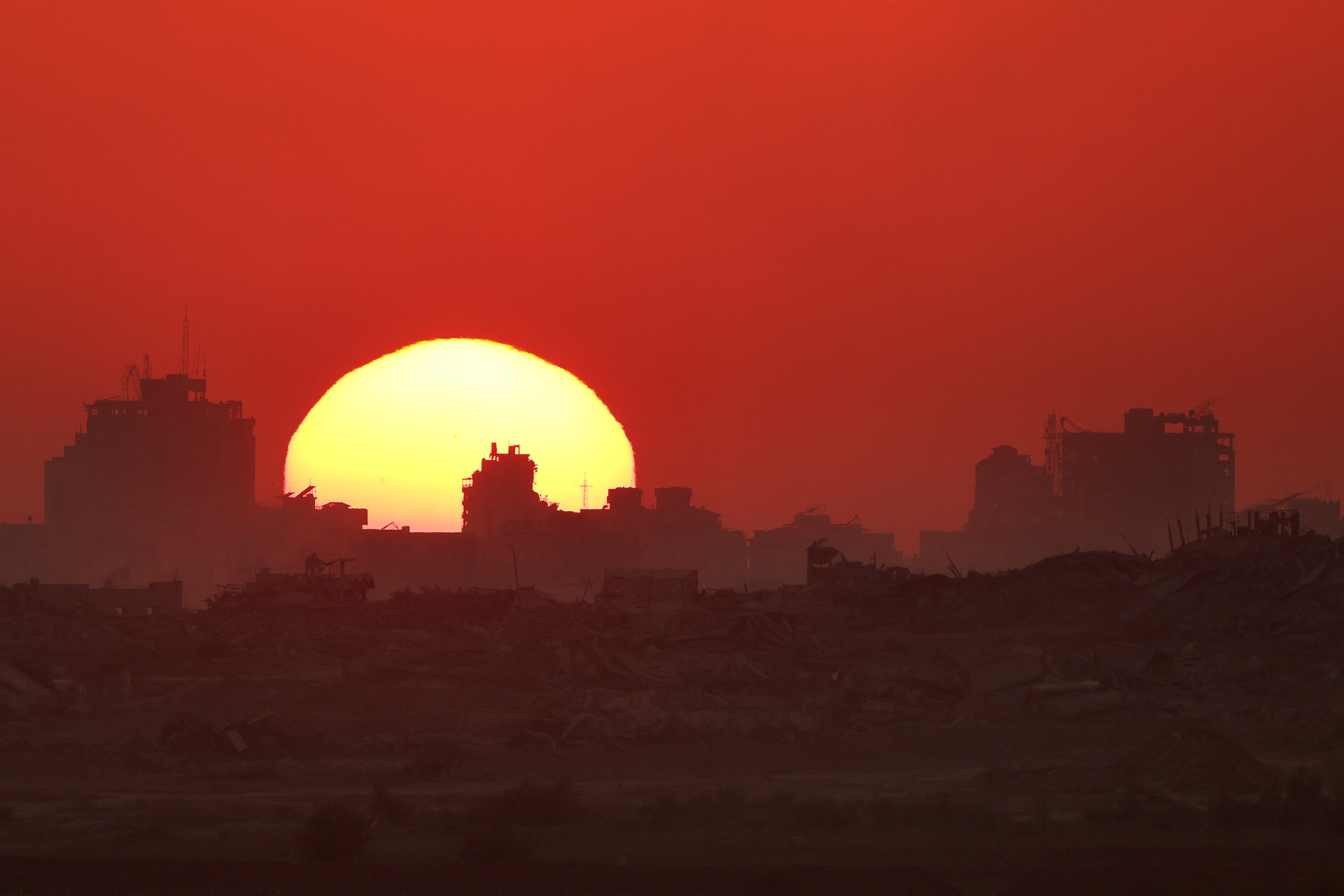 Foto tirada de um local na fronteira de Israel com a Faixa de Gaza, em 23 de julho de 2025, mostra o pôr do sol atrás de prédios destruídos dentro do território palestino sitiado (Foto: Jack GUEZ / AFP)