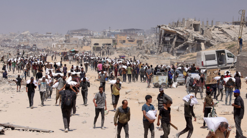 Pessoas caminham com sacos de farinha entregues após caminhões com ajuda humanitária entrarem no norte de Gaza em 27 de julho de 2025, vindos da passagem de fronteira de Zikim 