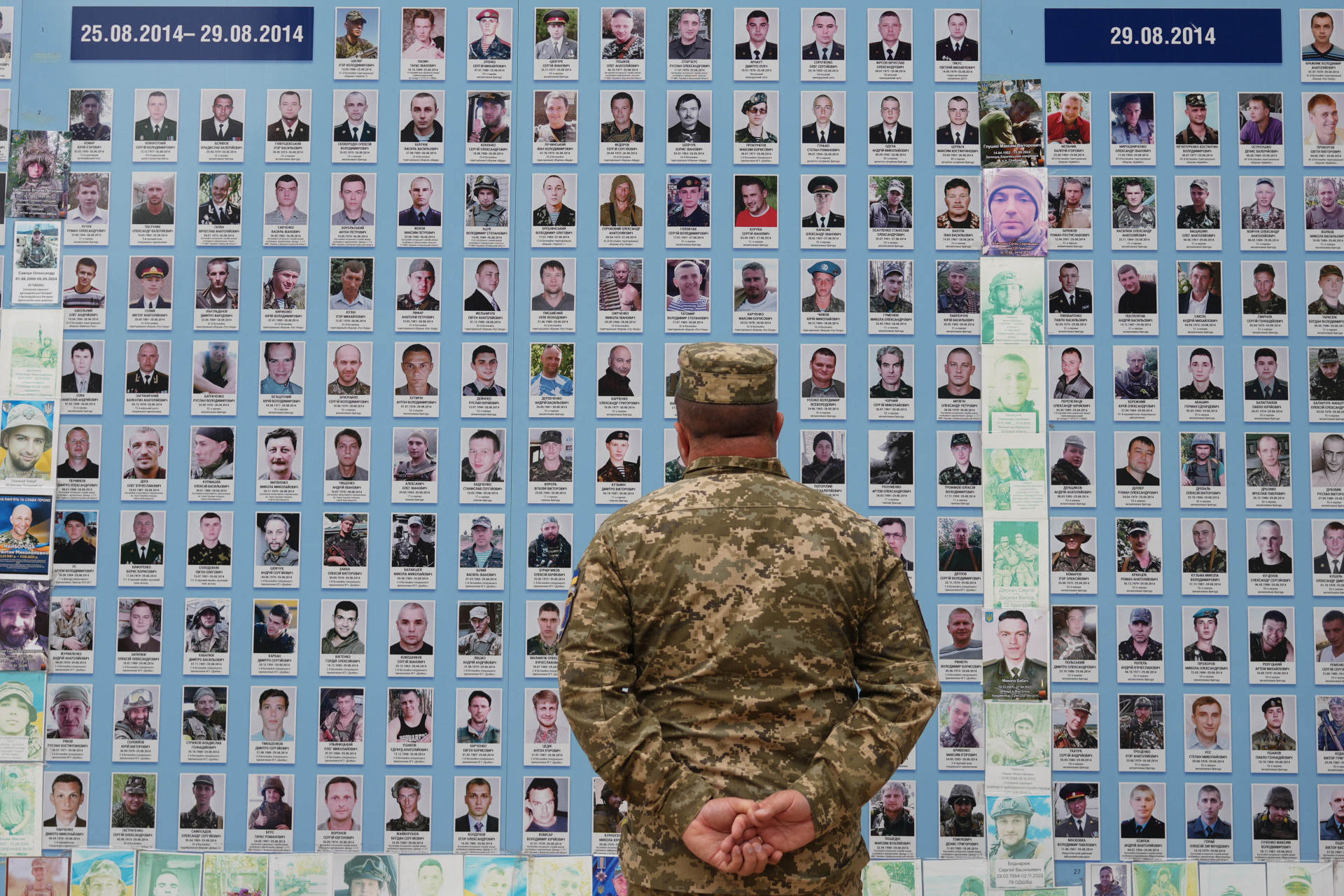 Um militar olha para fotografias de companheiros mortos no "Muro em Memória dos Mortos pela Ucrânia" no Dia da Independência da Ucrânia, em Kiev, em 24 de agosto de 2025 (Foto: OLEKSII FILIPPOV / AFP)