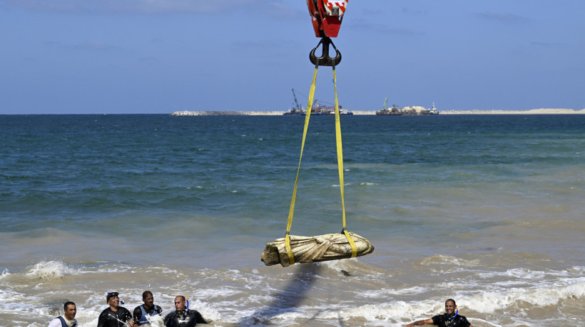 Mergulhadores observam um guindaste retirar um artefato das águas da baía de Abu Qir, em Alexandria, em 21 de agosto de 2025, como parte de um evento organizado pelo Ministério do Turismo e Antiguidades para recuperar antiguidades submersas