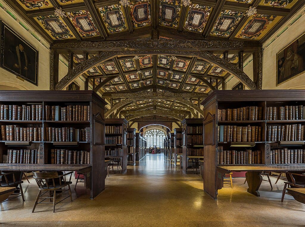 Duke Humphrey’s Library – Universidade de Oxford, Reino Unido – parte mais antiga da Bodleian Library, remonta ao século XV, com estantes de carvalho centenárias e painéis de teto pintados que conferem aura de scriptorium medieval.