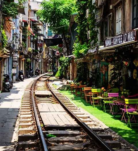 Trata-se de uma linha férrea colonial ainda em funcionamento que passa extremamente perto de cafés e casas em uma rua estreita da cidade.