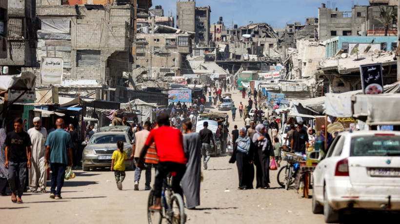 Pessoas passam por pr&eacute;dios danificados em uma rua em Khan Yunis, no sul da Faixa de Gaza, em setembro de 2025