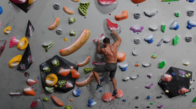 Atleta praticando a escalada em uma parede boulder, na Café com Magnésio