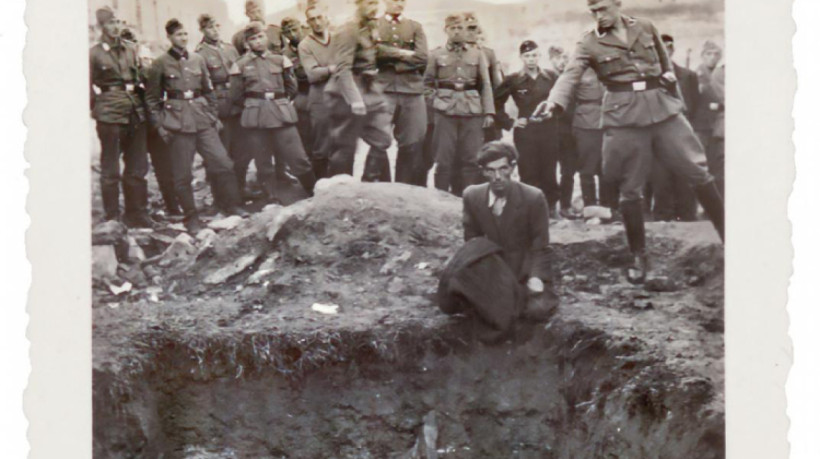A imagem mostra um homem agachado em frente a uma vala cheia de cadáveres, prestes a ser alvejado por um tiro de pistola, a ser disparado por um oficial alemão, durante o Holocausto, na Ucrânia, em 1941